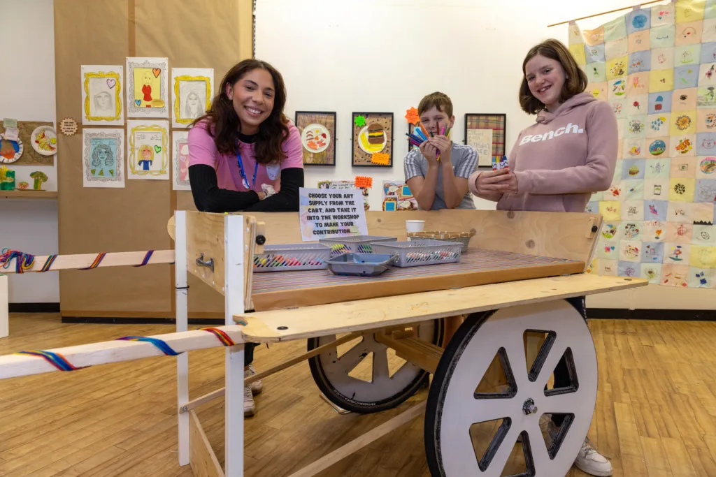 A mixed race woman and two white children lean on a decorated wooden cart